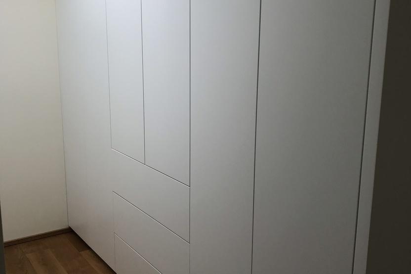 Ein großer weißer Einbauschrank nach Maß in einer Ecke, der perfekt zu dem hellen Holzboden und der schlichten Wand passt.