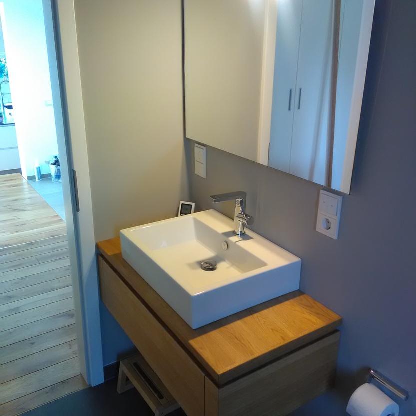 Ein zeitgenössisches Badezimmer mit einer maßgefertigten hölzernen Waschtischkonsole und einem rechteckigen Aufsatzbecken, flankiert von einem großen Spiegel und moderner Beleuchtung.