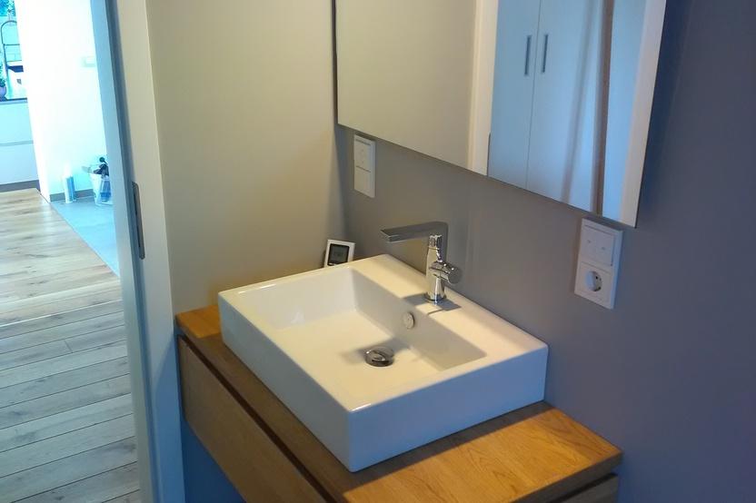 Ein zeitgenössisches Badezimmer mit einer maßgefertigten hölzernen Waschtischkonsole und einem rechteckigen Aufsatzbecken, flankiert von einem großen Spiegel und moderner Beleuchtung.