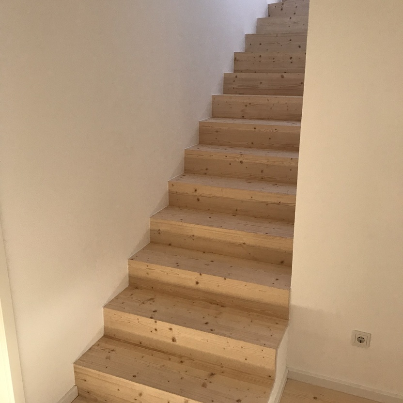 Eine gerade, maßangefertigte Treppe aus hellem Holz, die sich nach oben erstreckt, mit passenden Holzdielen als Bodenbelag.