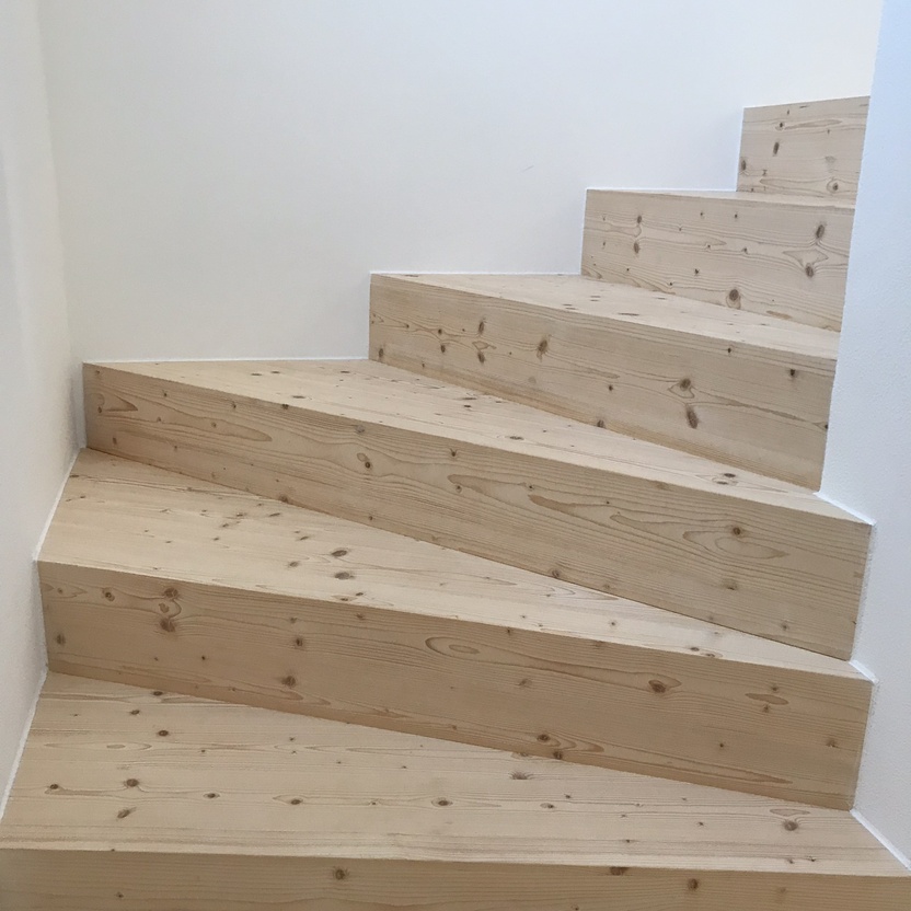 Blick auf eine aufsteigende Treppe nach Maß aus hellem Kiefernholz, eingebettet in ein minimalistisches weißes Raumdesign.