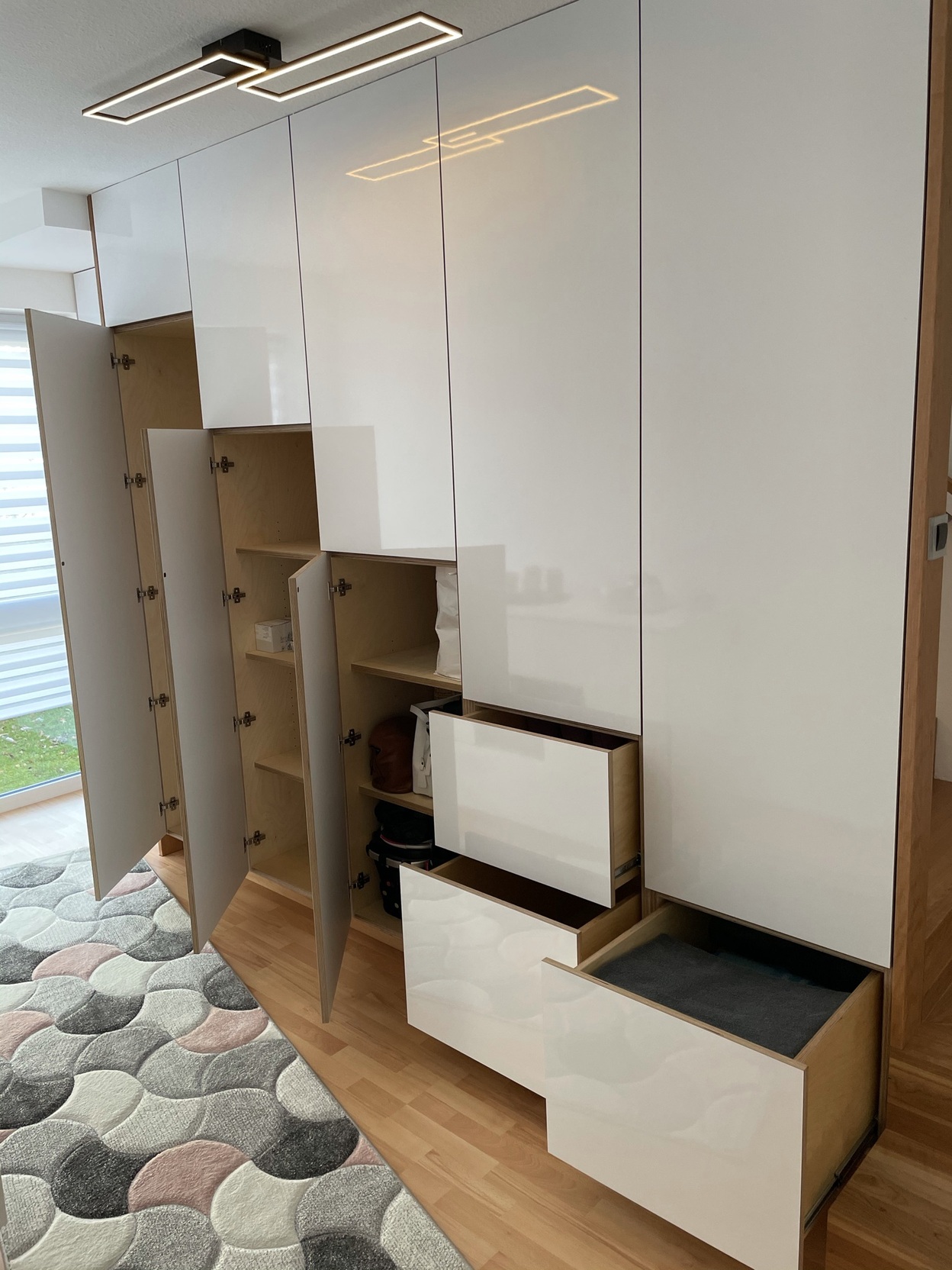 Moderne, maßgefertigte Einbaumöbel mit offenen Schubladen und Türen, die Stauraum in einem hellen Raum zeigen.