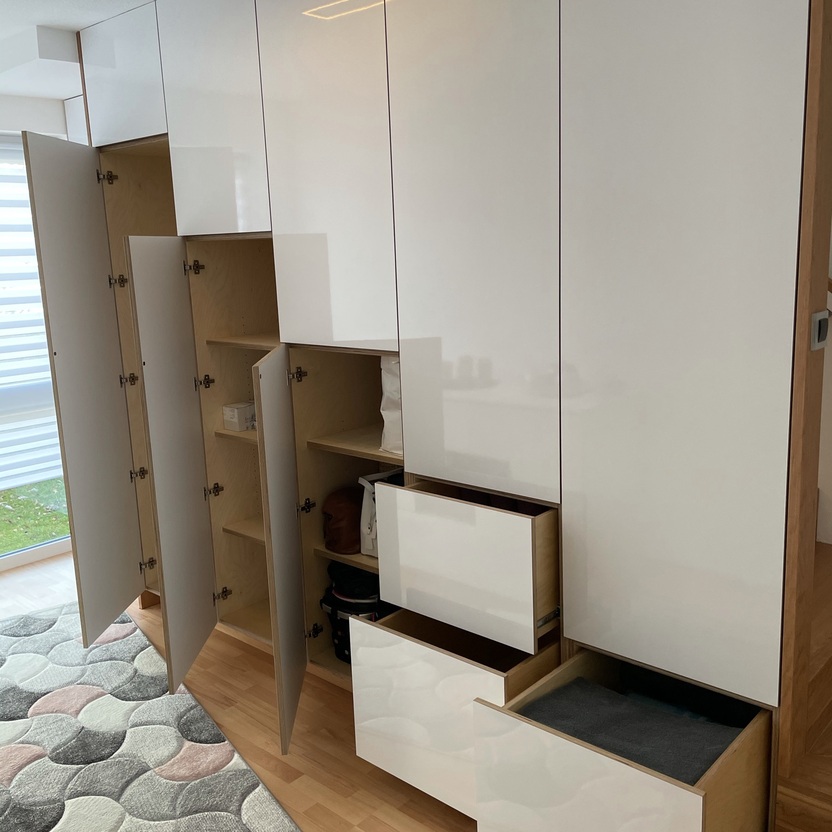 Moderne, maßgefertigte Einbaumöbel mit offenen Schubladen und Türen, die Stauraum in einem hellen Raum zeigen.