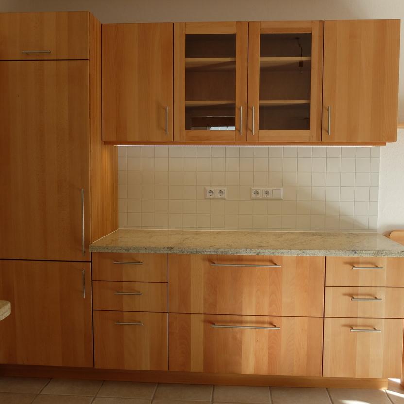 Küche nach Maß mit hellen Holzschränken, transparenten Oberschranktüren und einer Arbeitsplatte aus Granit, neben einer Sitzbank aus Holz.