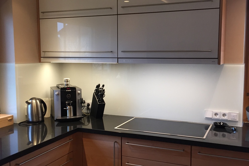 Maßgefertigte Kücheneinheit mit hellen Schrankfronten, schwarzer Arbeitsplatte, Einbaukaffeemaschine und Küchenutensilien.