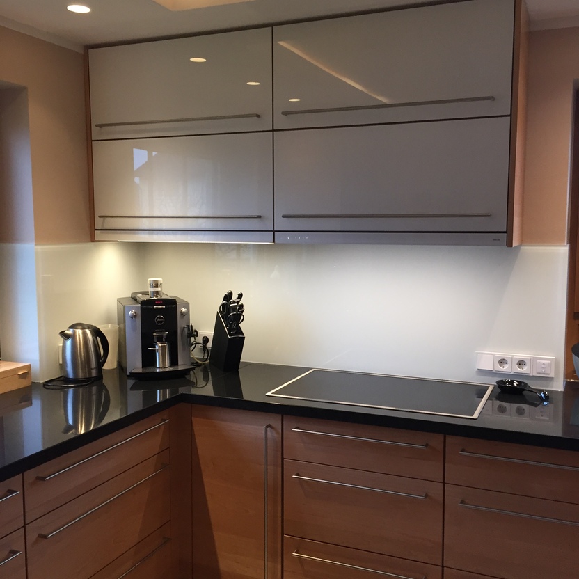 Maßgefertigte Kücheneinheit mit hellen Schrankfronten, schwarzer Arbeitsplatte, Einbaukaffeemaschine und Küchenutensilien.