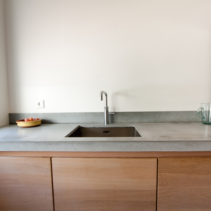 Ein moderner Küchenbereich nach Maß mit einer Betonarbeitsplatte, integriertem Spülbecken und hölzernen Unterschränken.