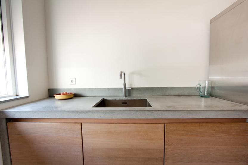 Ein moderner Küchenbereich nach Maß mit einer Betonarbeitsplatte, integriertem Spülbecken und hölzernen Unterschränken.