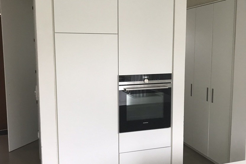Eine Hochglanz-weiße Kücheneinheit nach Maß mit eingebautem Ofen und Stauraum, in einem minimalistischen Küchendesign.
