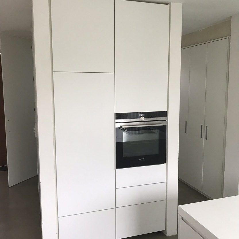 Eine Hochglanz-weiße Kücheneinheit nach Maß mit eingebautem Ofen und Stauraum, in einem minimalistischen Küchendesign.