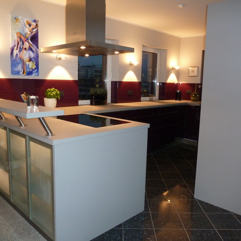 Moderne Küche nach Maß mit dunklen Unterschränken, gläserner Bartheke und stimmungsvoller Wandbeleuchtung.