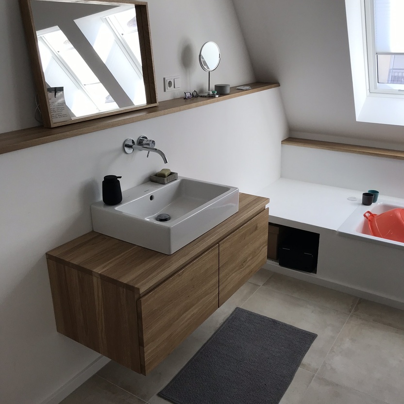 Ein helles, nach Maß gestaltetes Badezimmer mit einer hölzernen Waschtischkonsole, rechteckigem Spiegel und einer schlichten Badewanne.