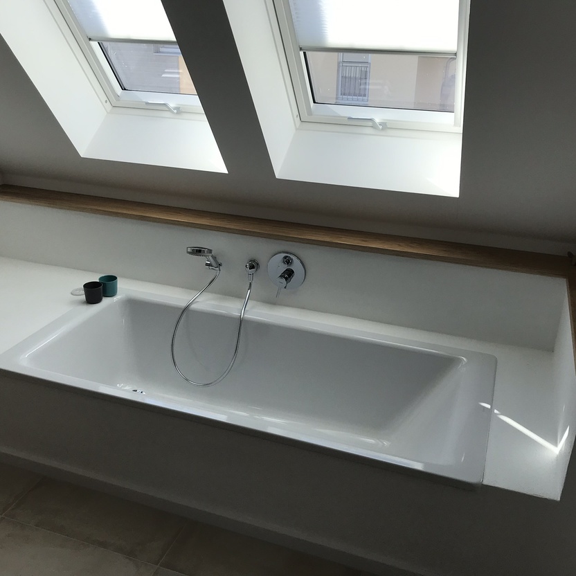 Ein individuell gestaltetes Bad mit einer Einbauwanne unter Dachfenstern und einer Ablage aus Holz für eine natürliche Atmosphäre.