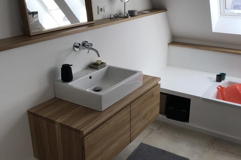 Ein helles, nach Maß gestaltetes Badezimmer mit einer hölzernen Waschtischkonsole, rechteckigem Spiegel und einer schlichten Badewanne.