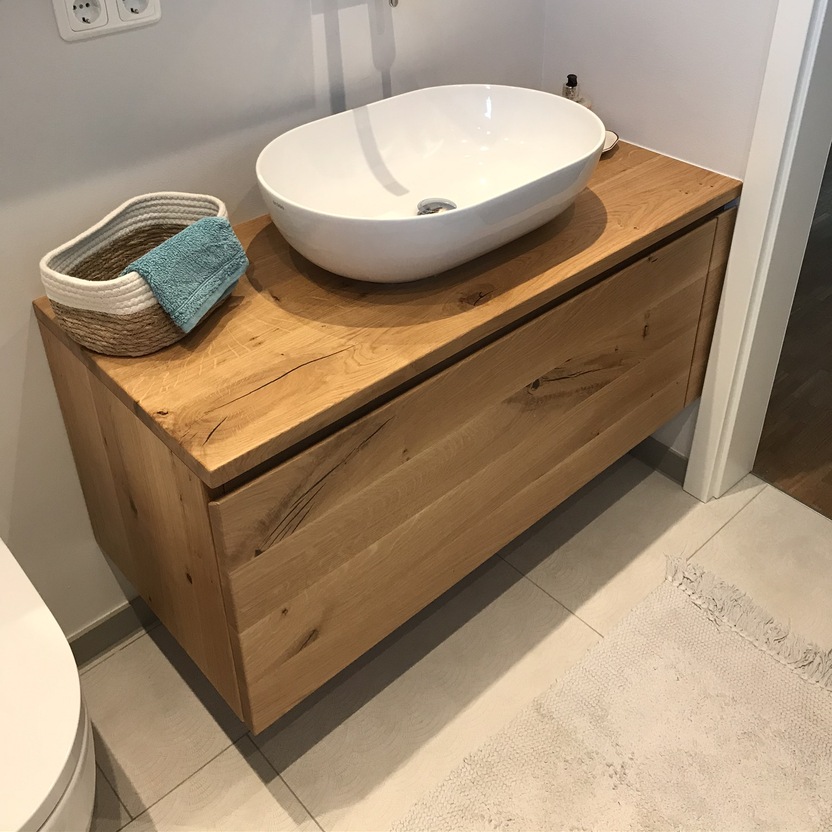 Ein stilvolles Bad nach Maß mit einem ovalen Aufsatzwaschbecken auf einer hölzernen Waschtischplatte und passendem Spiegel darüber.