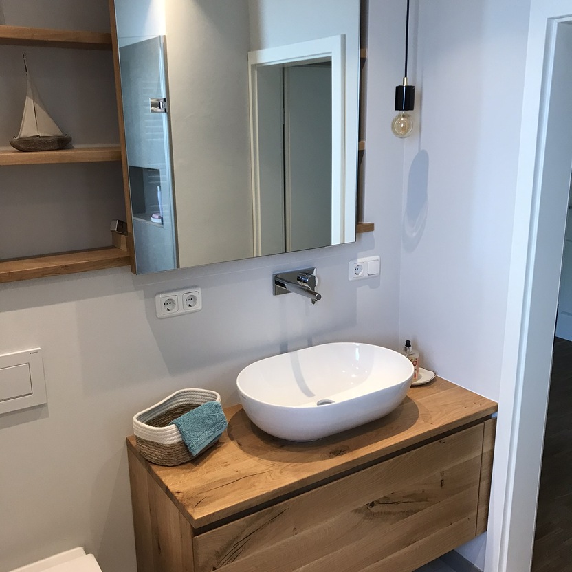 Modernes Badezimmer mit einem ovalen Aufsatzwaschbecken auf einem maßgefertigten Holzwaschtisch, ergänzt durch eine hängende Lampe und Spiegel.