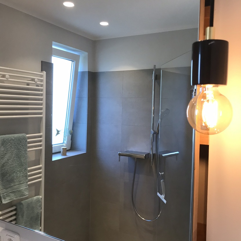 Modern gestaltetes Badezimmer mit einer großzügigen, maßgefertigten Dusche, grauen Fliesen und einer stilvollen Beleuchtung.