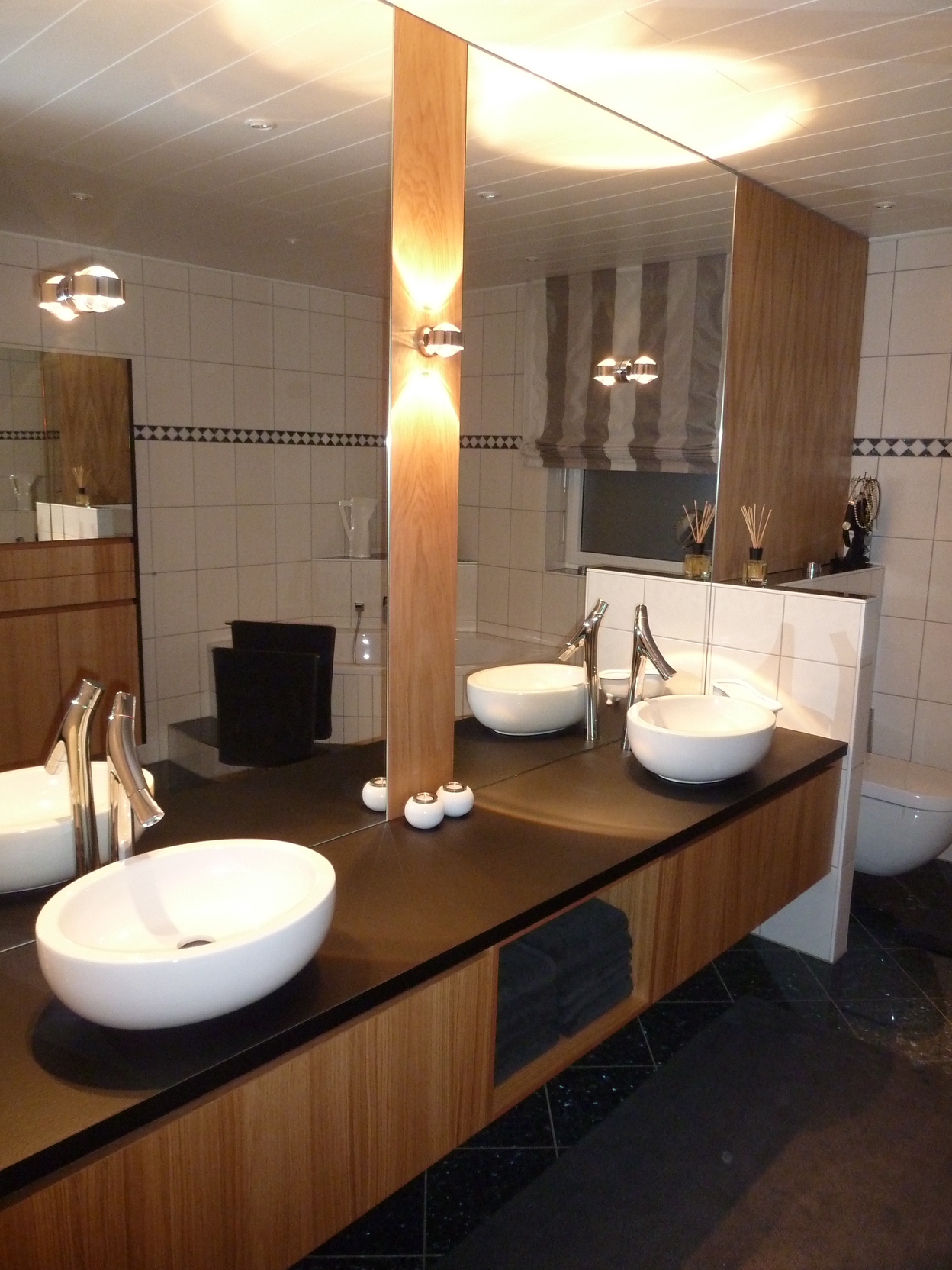 Ein modernes Bad nach Maß mit zwei ovalen Aufsatzwaschbecken, dunkler Ablagefläche und einem großen Spiegel.