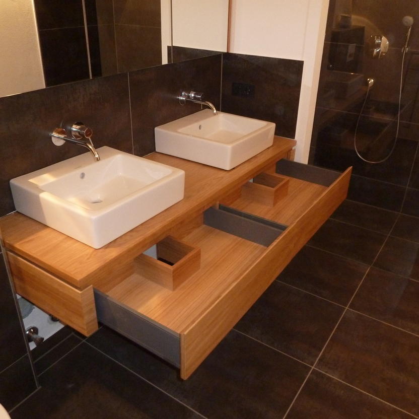 Eleganter Doppelwaschtisch aus Holz mit zwei rechteckigen Aufsatzbecken in einem dunkel gefliesten Badezimmer, maßgefertigte Badmöbel inklusive.