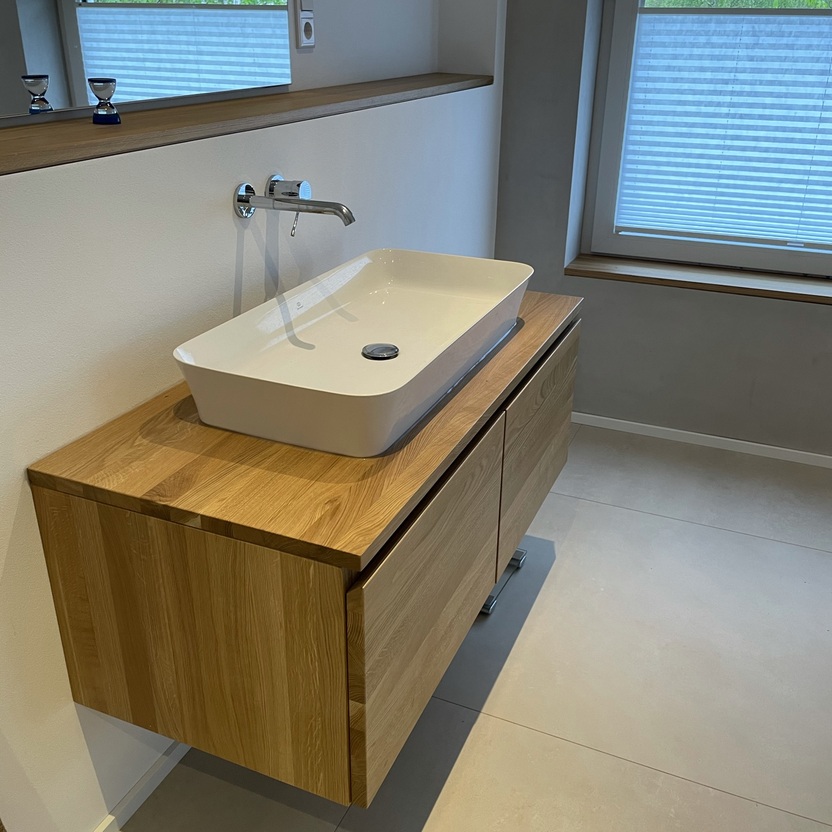 Stilvolles Badezimmer mit einem rechteckigen Aufsatzbecken auf einem maßgefertigten Holzwaschtisch, ergänzt durch eine minimalistische Armatur und einen Wandspiegel.