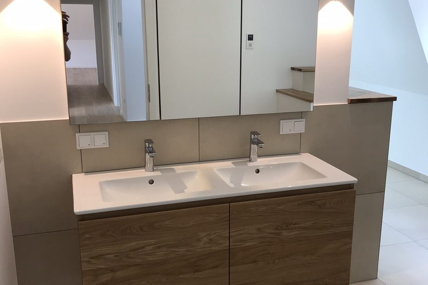 Elegantes Badezimmer mit einem Doppelwaschbecken und darunter befindlichen maßgefertigten Badmöbeln aus Holz, ergänzt durch einen großen Spiegelschrank.