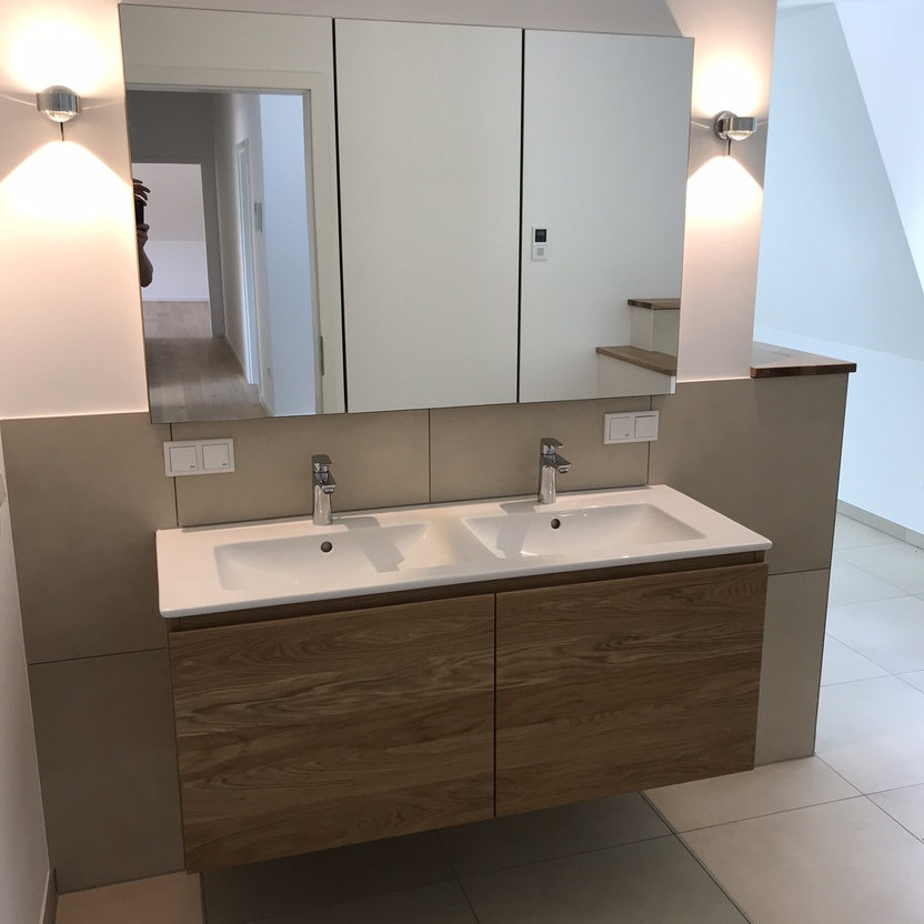 Elegantes Badezimmer mit einem Doppelwaschbecken und darunter befindlichen maßgefertigten Badmöbeln aus Holz, ergänzt durch einen großen Spiegelschrank.