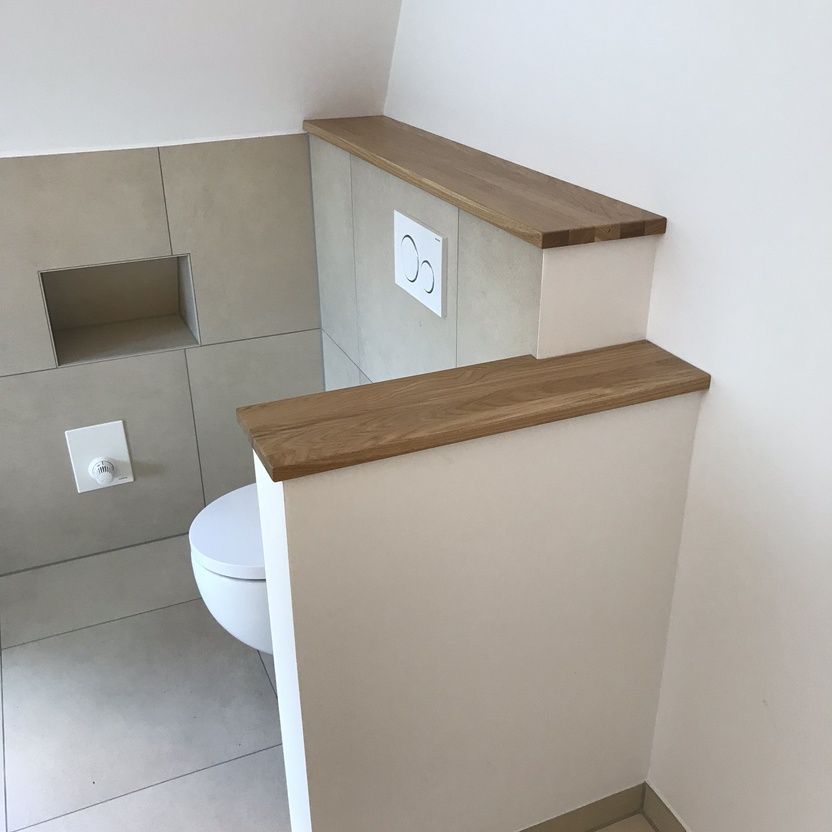 Modernes Badezimmer mit einer maßgefertigten Toilettenumrandung aus hellem Holz und weißem Dekor, ergänzt durch praktische Ablagen.