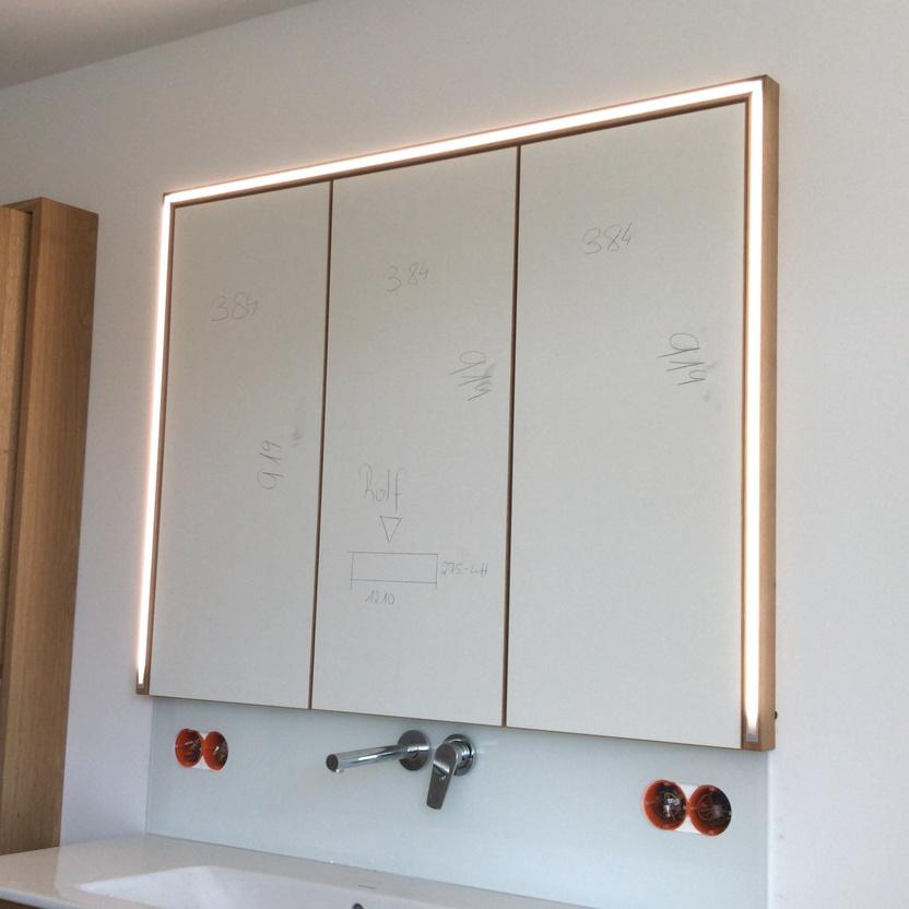 Moderne Badmöbel nach Maß in einem Badezimmer, einschließlich eines Spiegelschranks mit Messmarkierungen und unteren Schubladenelementen.