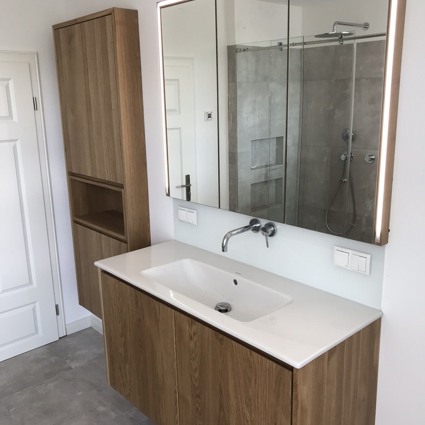 Ein modernes Badezimmer mit Badmöbeln nach Maß, darunter ein Waschtisch aus Holz mit darüber liegendem Spiegelschrank und integrierter Beleuchtung.