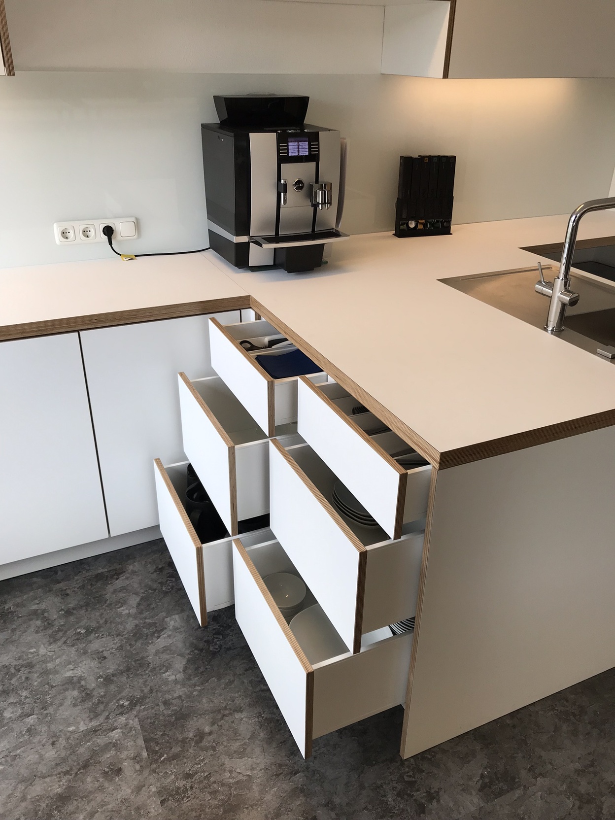 Praktische Büro-Teeküche mit geöffneten Schubladen, Geschirr und Kaffeemaschine als funktionale Büromöbel nach Maß