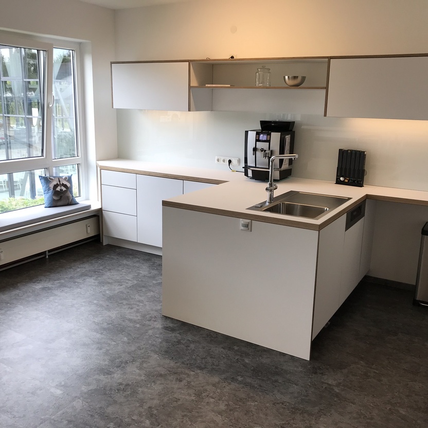 Helles, minimalistisch eingerichtetes Büro mit modernen Büromöbeln, darunter eine Küchenzeile mit Einbauschränken und Geräten.