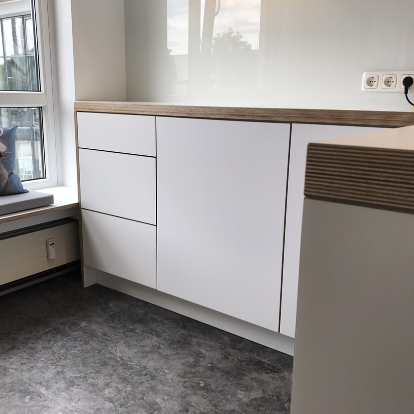 Nahaufnahme von modernen Büromöbeln in einer Büroküche, inklusive weißer Schränke und einer Fensterbank mit einem Kissen, auf dem ein Waschbär abgebildet ist.