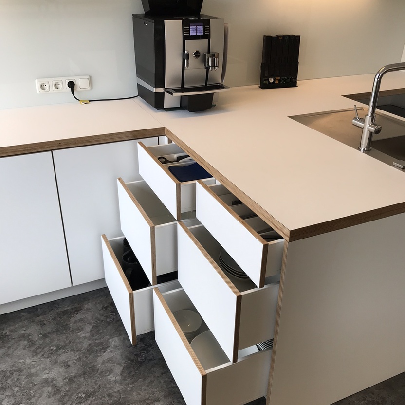 Praktische Büro-Teeküche mit geöffneten Schubladen, Geschirr und Kaffeemaschine als funktionale Büromöbel nach Maß