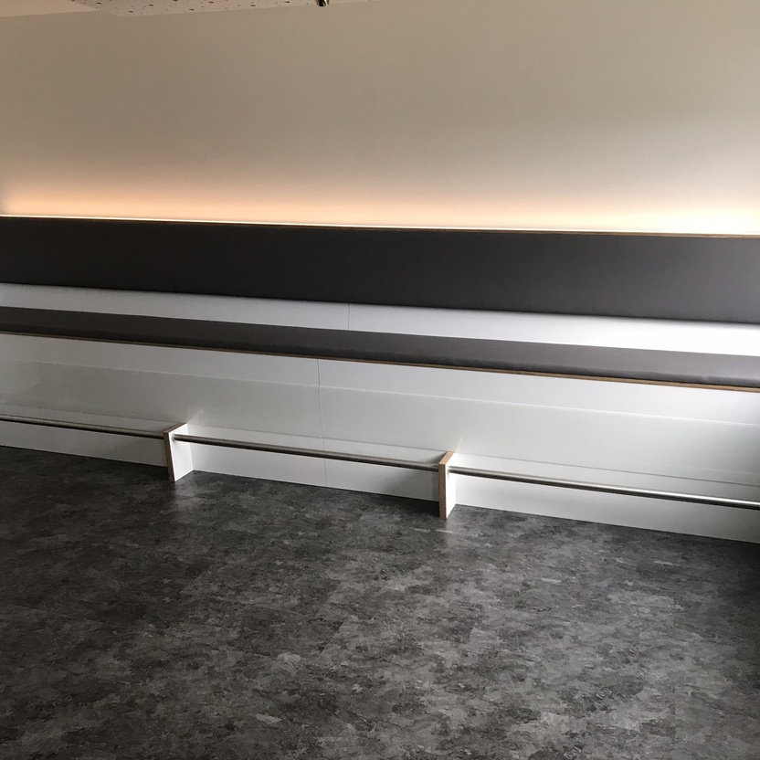 Lange Sitzbank mit Polsterung, integriertem Stauraum und indirekter Beleuchtung als moderne Büromöbel nach Maß
