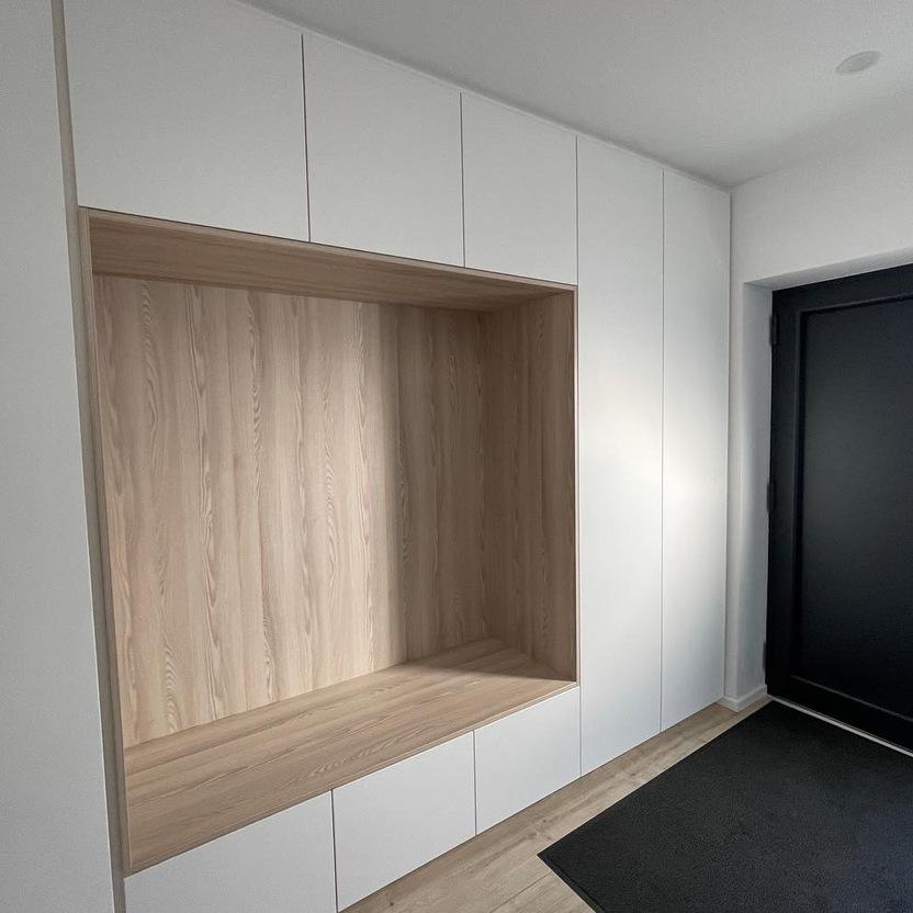 Großer, moderner Einbauschrank aus hellem Holz und weißen Türen im Flur eines Hauses, bietet sowohl Sitzgelegenheit als auch Stauraum.