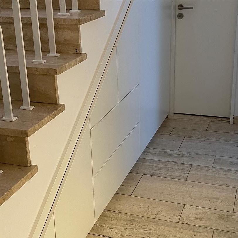 Maßgeschneiderter Einbauschrank in Weiß, der sich nahtlos unter die Stufen einer Holztreppe mit gedrehten Balustern einfügt.