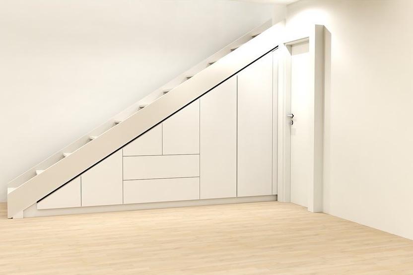 Maßgefertigter Einbauschrank in Weiß, integriert unter einer Treppe in einem Raum mit hellem Holzboden und neutraler Wandfarbe.