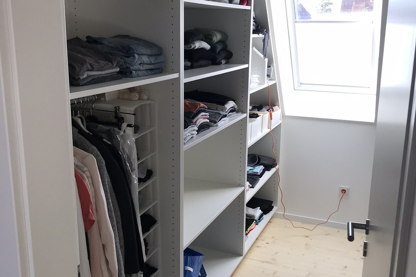 Ein geräumiger, offener Einbauschrank nach Maß mit Regalen und Kleiderstange, effizient in einer Dachschräge integriert.