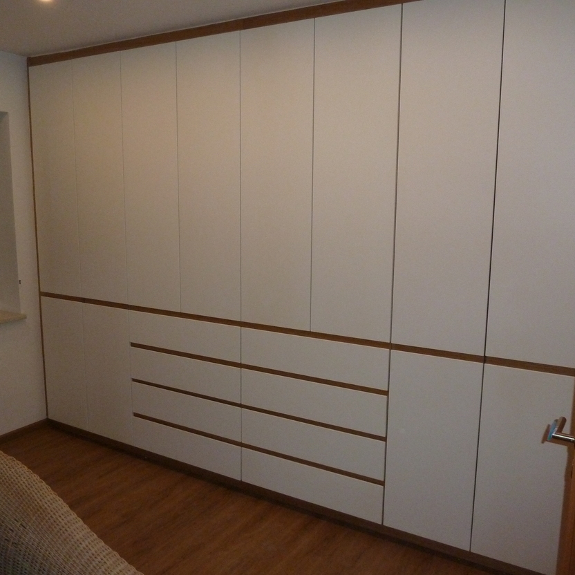 Ein großer, weißer Einbauschrank mit holzfarbenen Akzenten, der nahtlos in die Wand eines gemütlichen Wohnzimmers integriert ist.