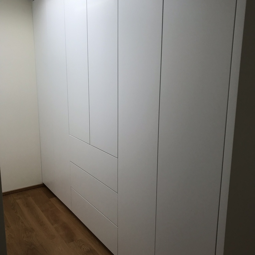 Ein großer weißer Einbauschrank nach Maß in einer Ecke, der perfekt zu dem hellen Holzboden und der schlichten Wand passt.