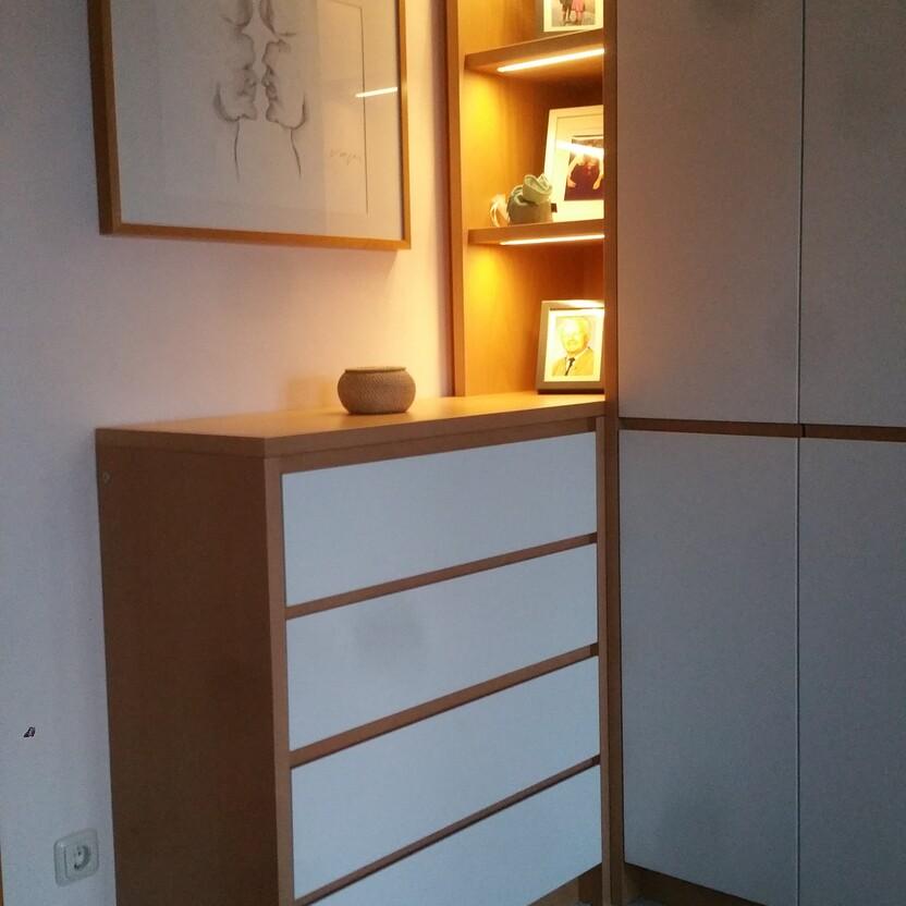 Ein Flur mit maßgefertigten Möbeln, beleuchteten Regalen und einer Kommode, ergänzt durch Kunst und einen orientalischen Teppich.