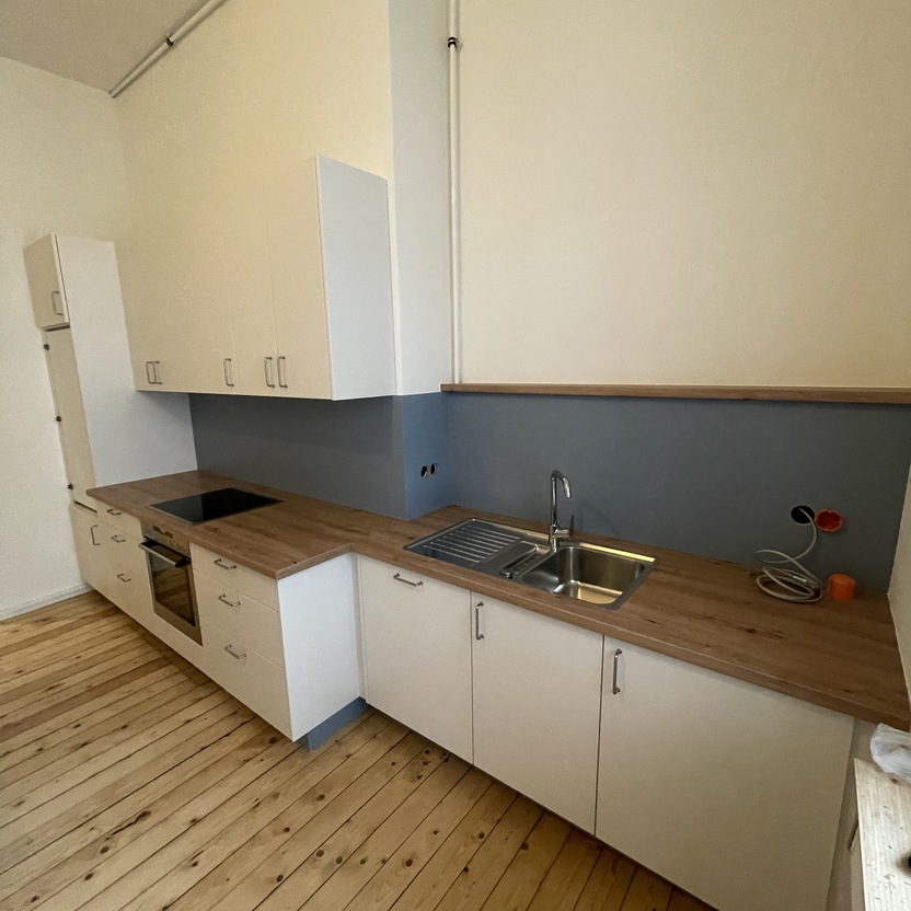 In Montage befindliche Küche nach Maß mit hellen Fronten, Holzarbeitsplatte und Einbauspüle auf einem rustikalen Holzboden.